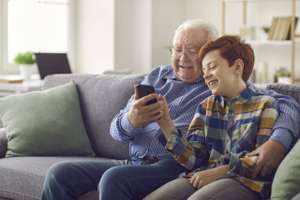 Grandson Showing Grandpa How To Use Social Media Or Make Video Call On Mobile Phone