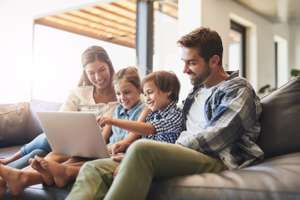 Connected Online And As A Family. Shot Of A Mother And Father Using A Laptop With Their Son And Daughter On The Sofa At Home.