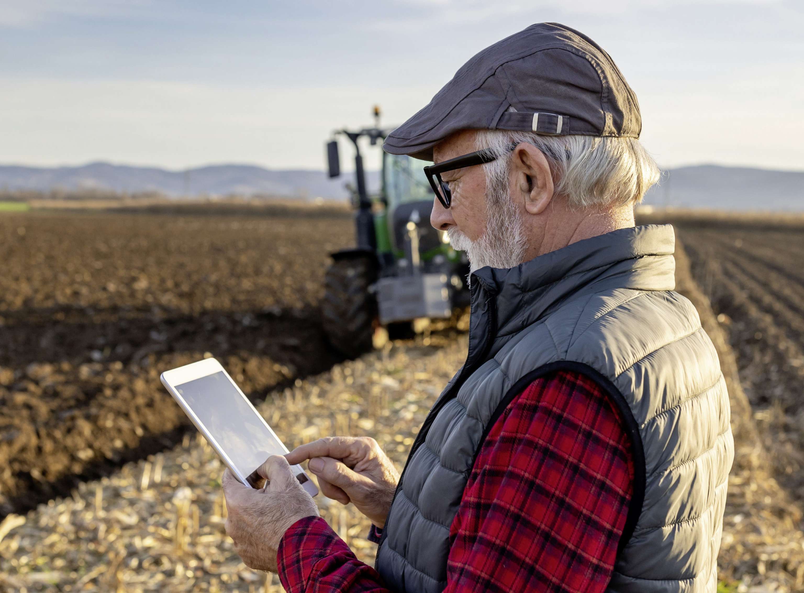 Senior Farmer With Tablet In Field With Tractor In Background