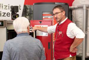 Mann in roter Weste erklärt einem älteren Mann ein technisches Gerät auf einer Messe mit dem Logo "Hargassner" im Hintergrund.
