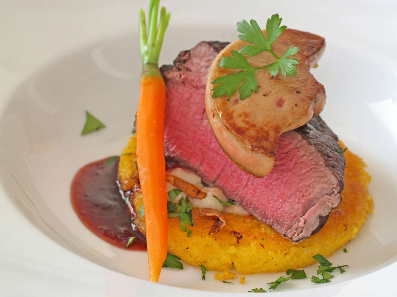 Elegantes Gericht: rosa gebratenes Rindfleisch auf Polenta mit Foie Gras, Karotte, Rotweinsoße und Petersilie.