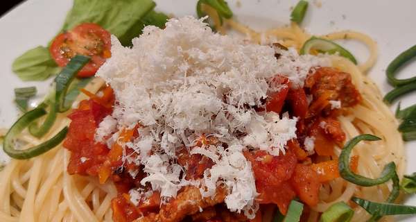 Spaghetti mit Kürbissauce, geriebenem Parmesan, Frühlingszwiebeln und Kirschtomaten auf weißem Teller, zweiter Teller im Hintergrund.