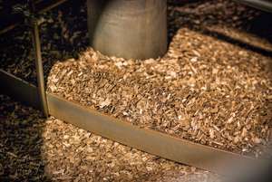 Close-up of a large pile of wood chips in a processing machine, with metal barriers surrounding the area.