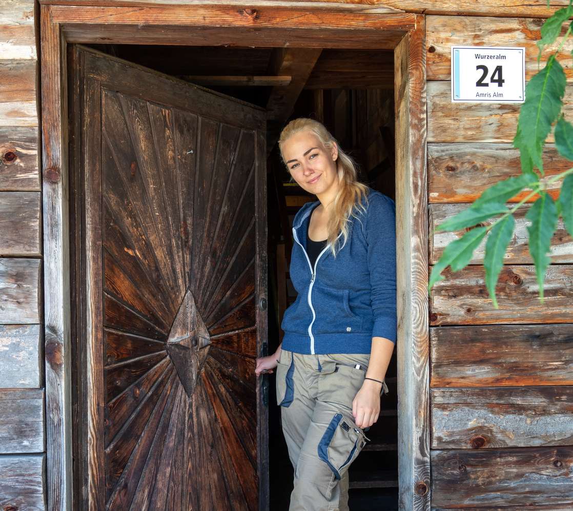 Junge Frau in blauer Jacke steht lächelnd an der Holztür der Wurzeralm Amris Alm Nr. 24.