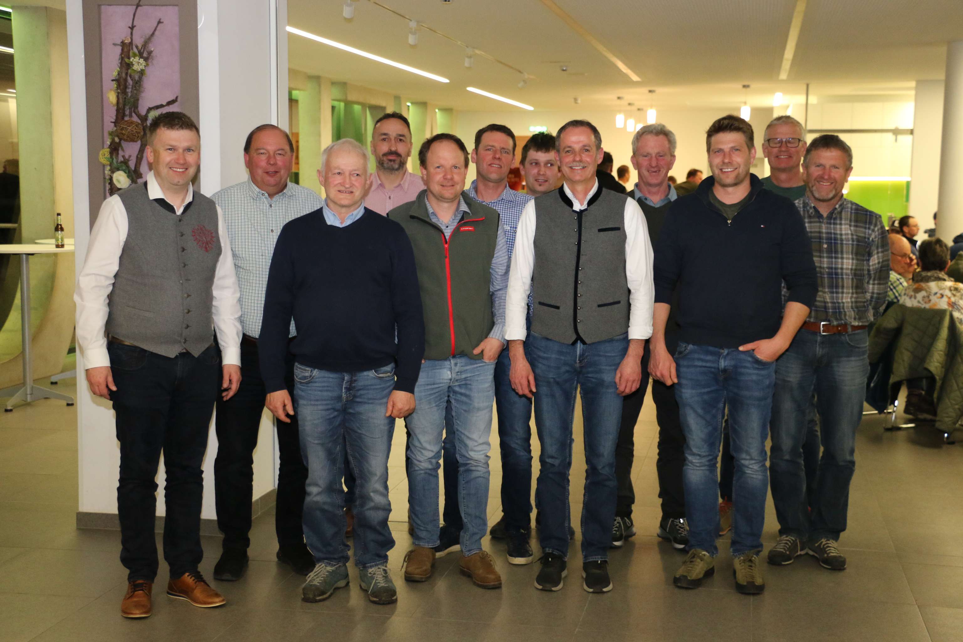 Gruppe von zwölf Männern, die lächelnd in Freizeitkleidung in einem modernen Raum stehen.