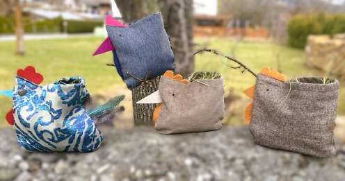 Handcrafted fabric chickens with various patterns and colors perched outdoors on a branch.