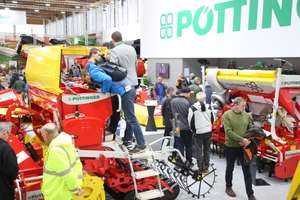Messestand von Pöttinger mit roten und gelben Landmaschinen, umgeben von zahlreichen Besuchern in einer Ausstellungshalle.