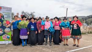 Indigene Frauen in bunter Tracht winken beim Projekt „Jugend Eine Welt" zur Agroökologie in Südamerika.