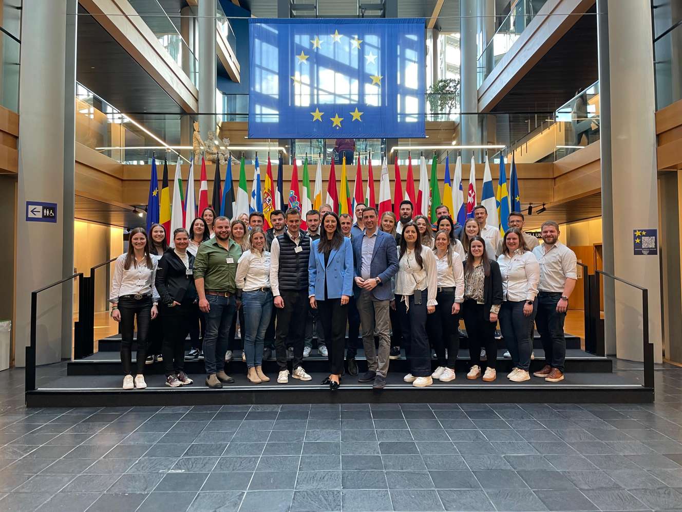 Eine Gruppe von Menschen steht vor den EU-Flaggen in einem modernen Gebäude.