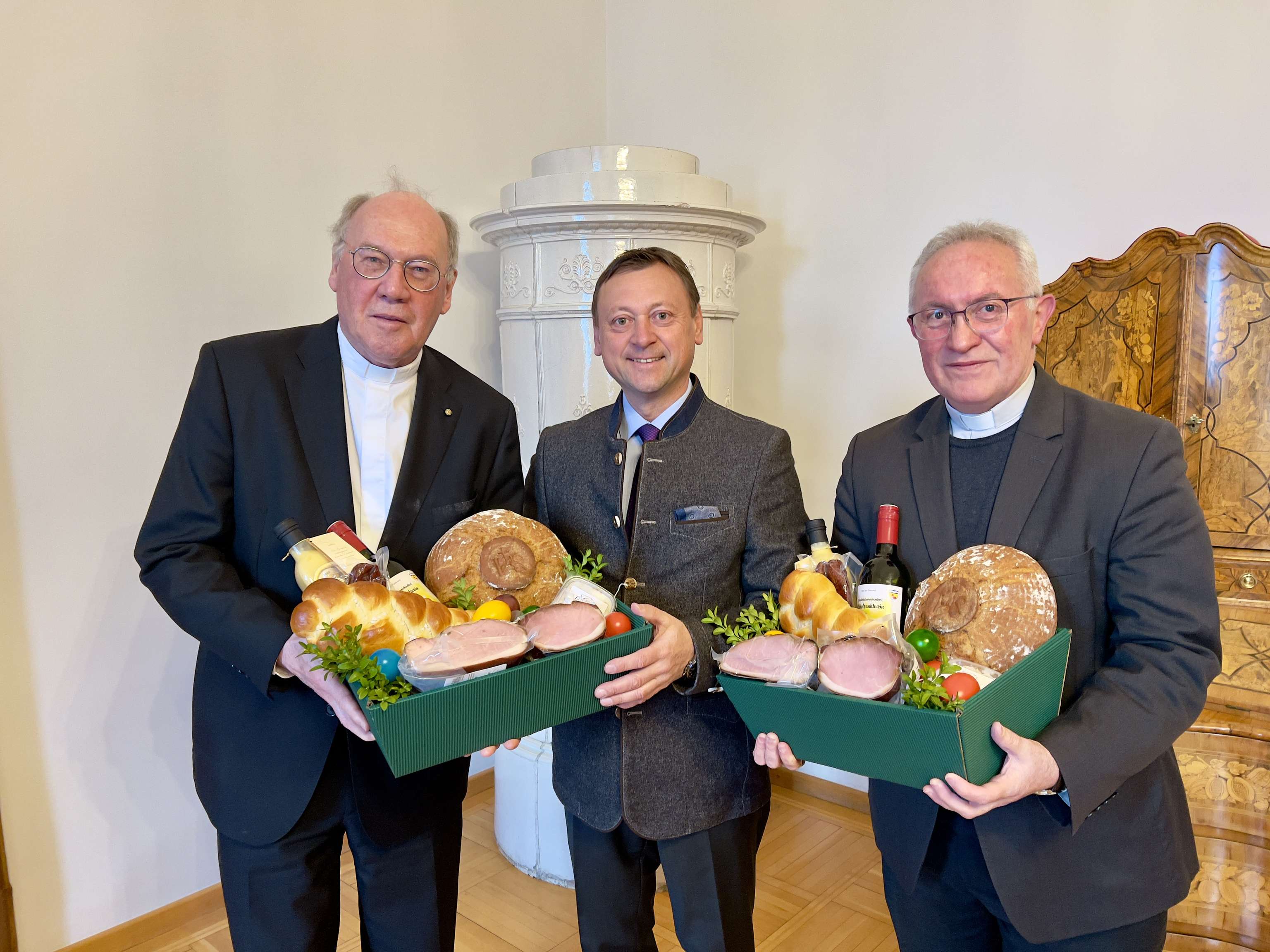 Johann Höfinger übergibt gefüllte Körbe mit Köstlichkeiten an Diözesanbischof Alois Schwarz und Weihbischof Anton Leichtfried.
