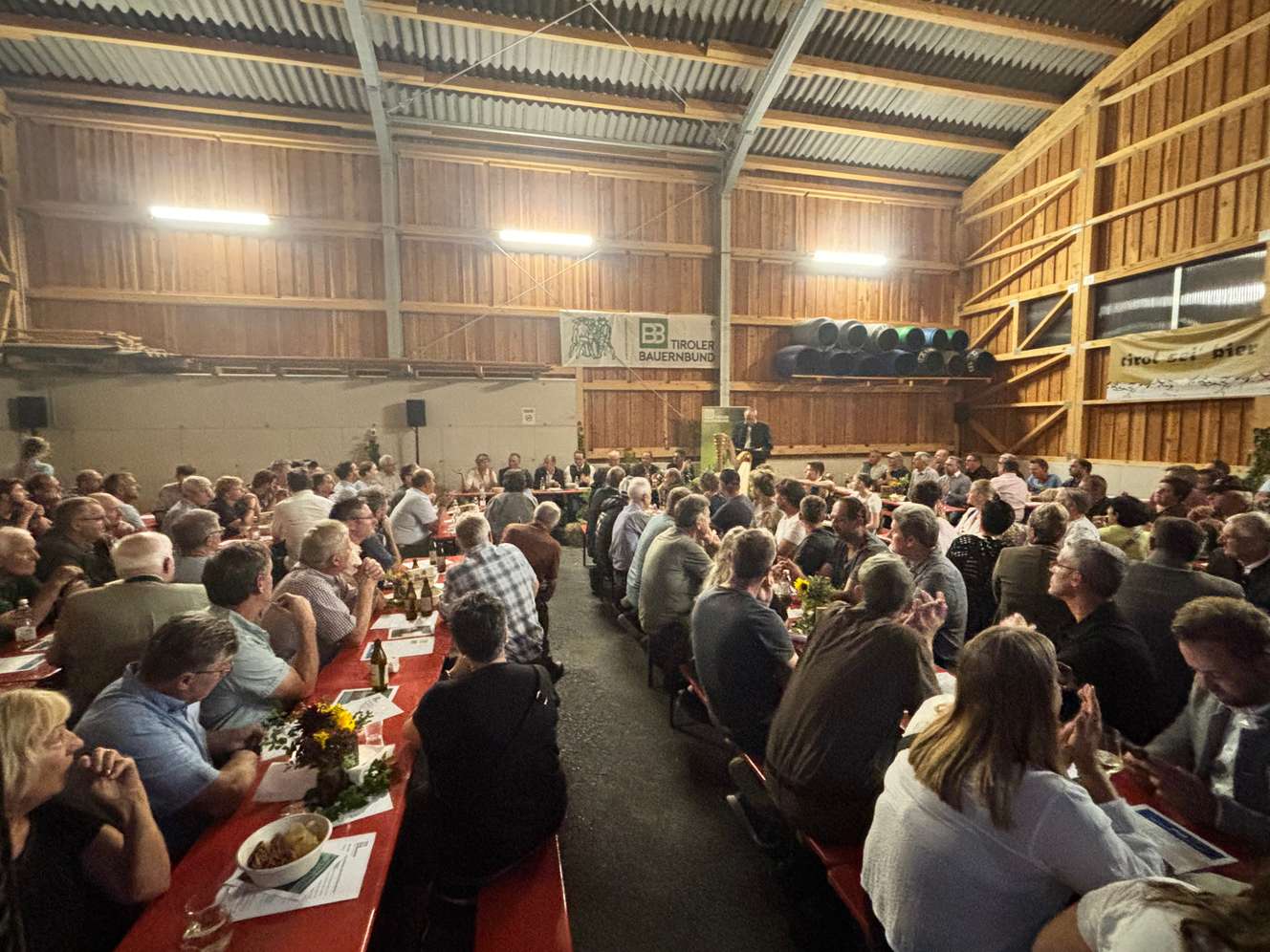 Vollbesetzte Veranstaltung des Tiroler Bauernbundes in einer Holzhalle mit vielen Besuchern an langen Tischen.