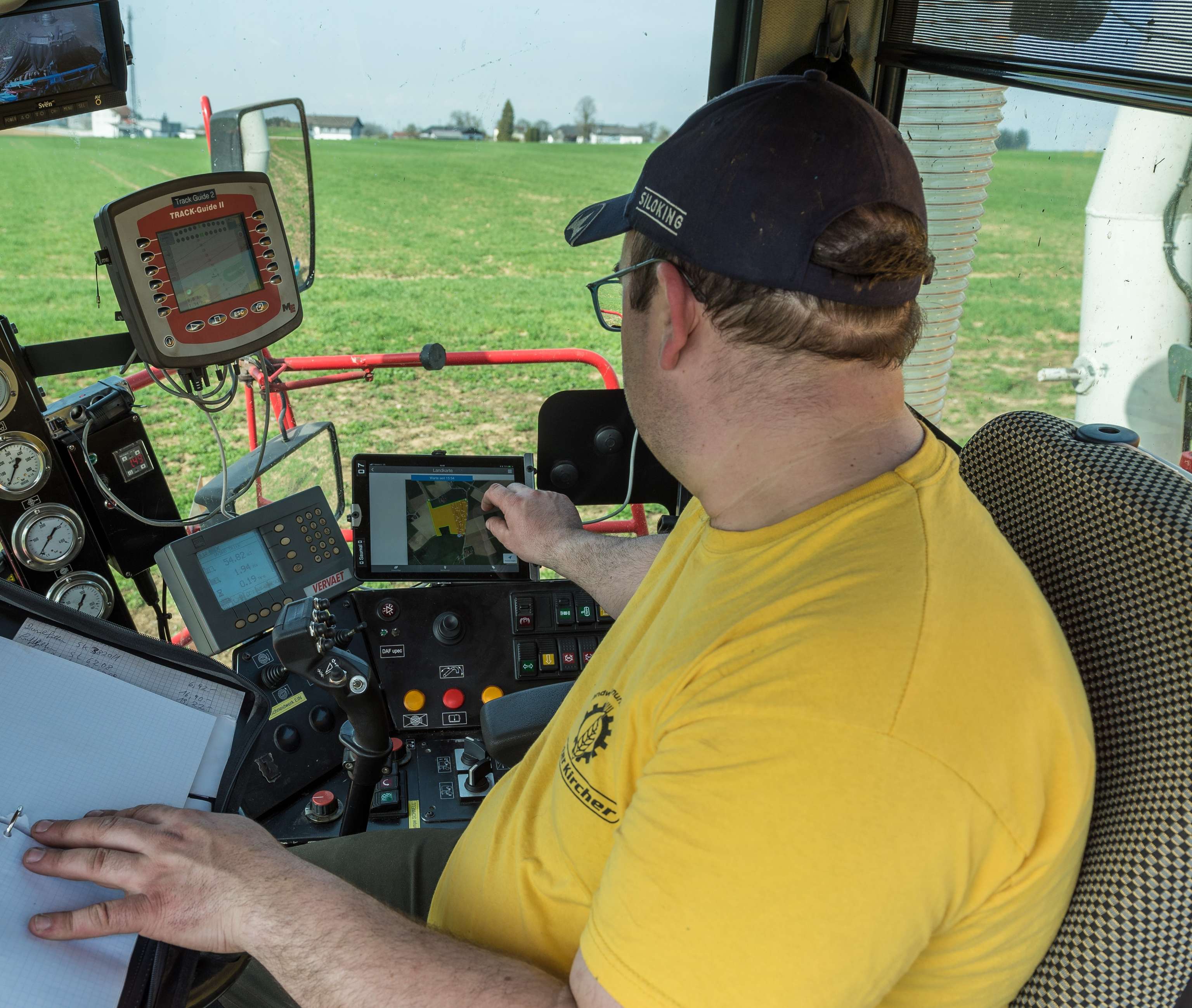 Landwirt in gelben T-Shirt bedient Tablet mit GPS-Karte in moderner Traktorkabine mit digitalen Steuergeräten und Feldblick.