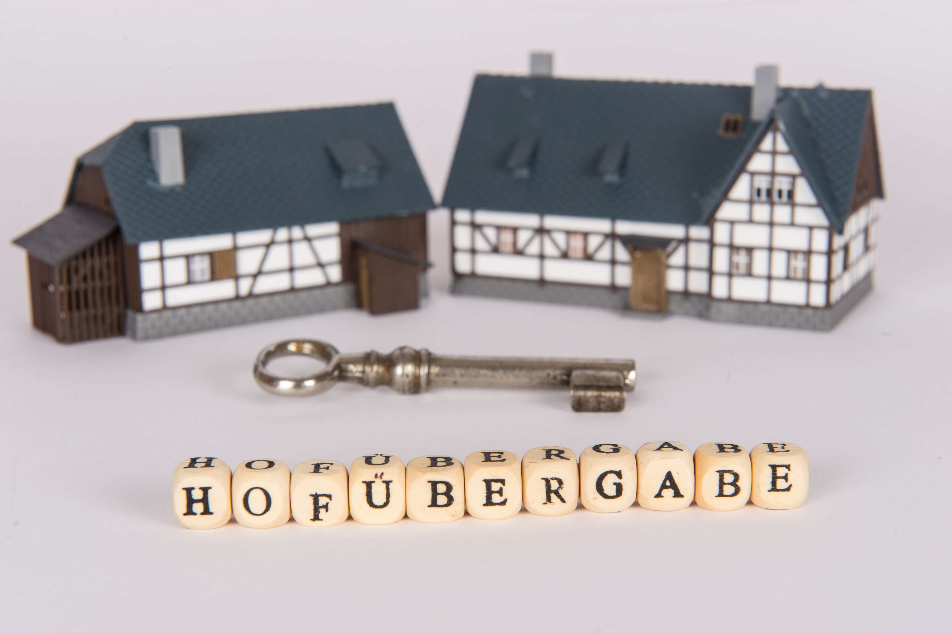 Zwei Spielzeug-Bauernhäuser mit einem Schlüssel und dem Schriftzug "Hofübergabe" davor.