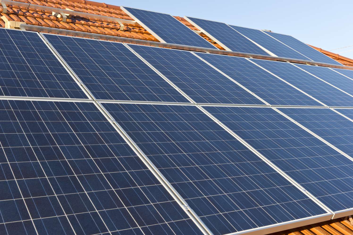 Blaue Solarpanele auf einem Hausdach mit roten Ziegeln unter klarem Himmel – Photovoltaikanlage zur Stromerzeugung.