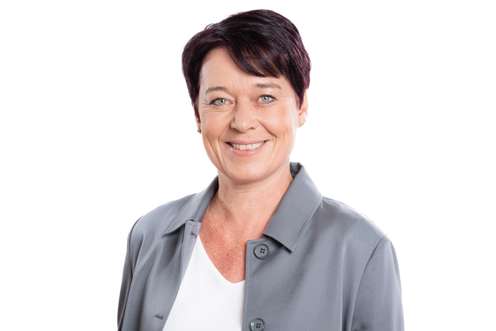 Lächelnde Frau mit kurzen dunkelroten Haaren und blauen Augen in grauer Jacke, professionelles Porträtfoto vor weißem Hintergrund.