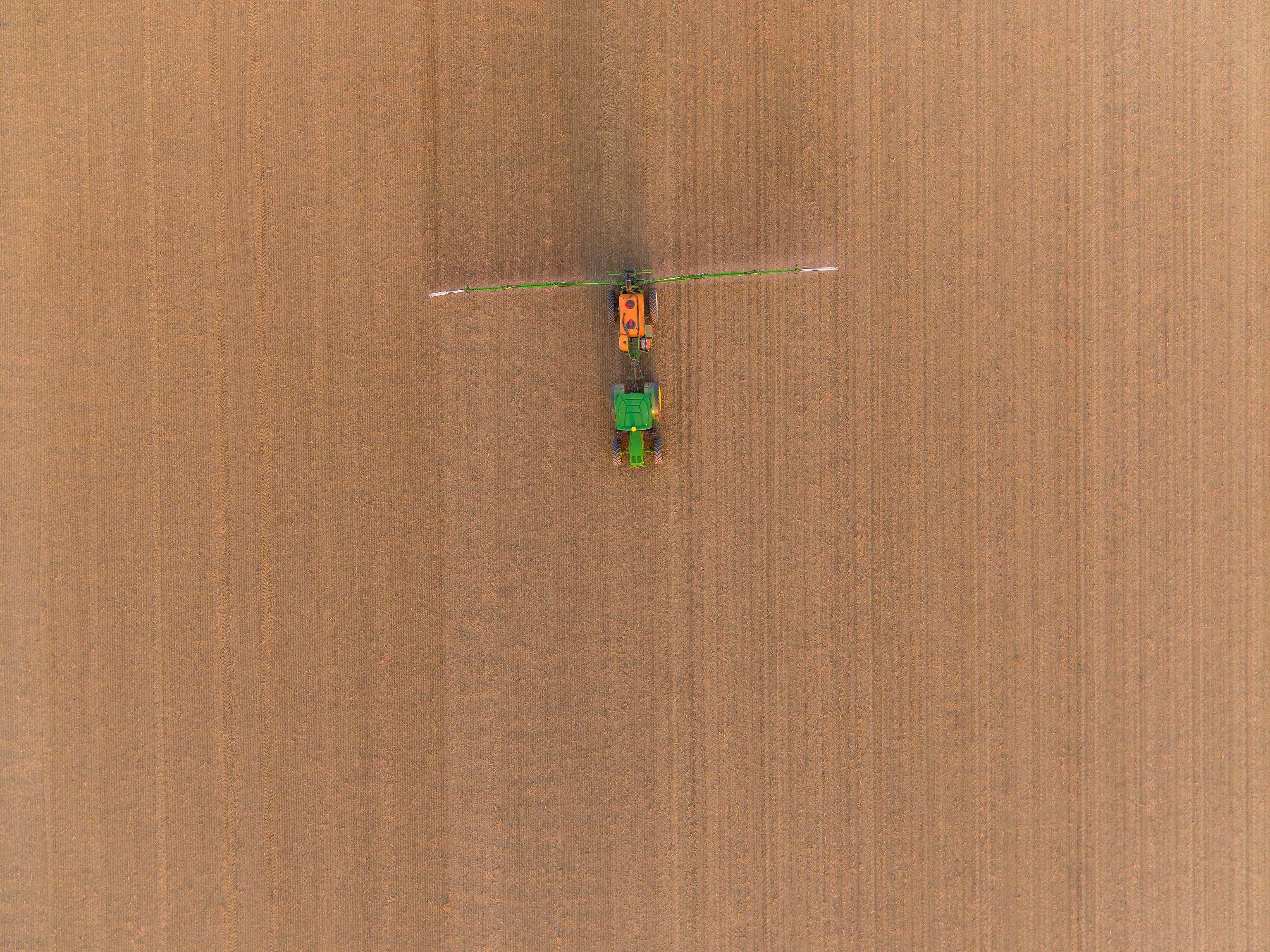 Traktor fährt mit Feldspritze über ein noch unbestelltes Feld