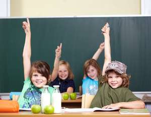 Schulkinder in der Klasse melden sich per Handzeichen.