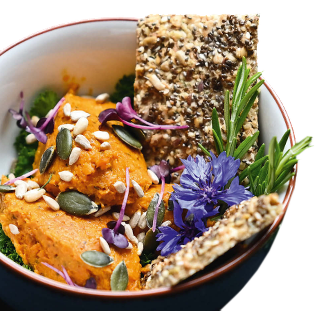 Schale mit orangener Creme, garniert mit Samen, essbaren Blumen, Kräutern und knusprigem Knäckebrot.