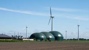 Drei Bioreaktoren auf einer Freifläche, dahinter Windräder