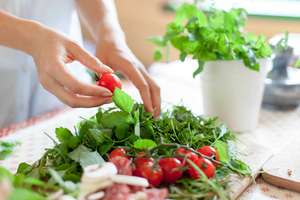 Woman Is Cooking In Home Kitchen. Female Hands Choose Cherry Tomatoes, Vegetables For Recipe. Ingredients For Preparing Italian Or French Food Are On Table On Wooden Boards. Lifestyle Moment. Close Up