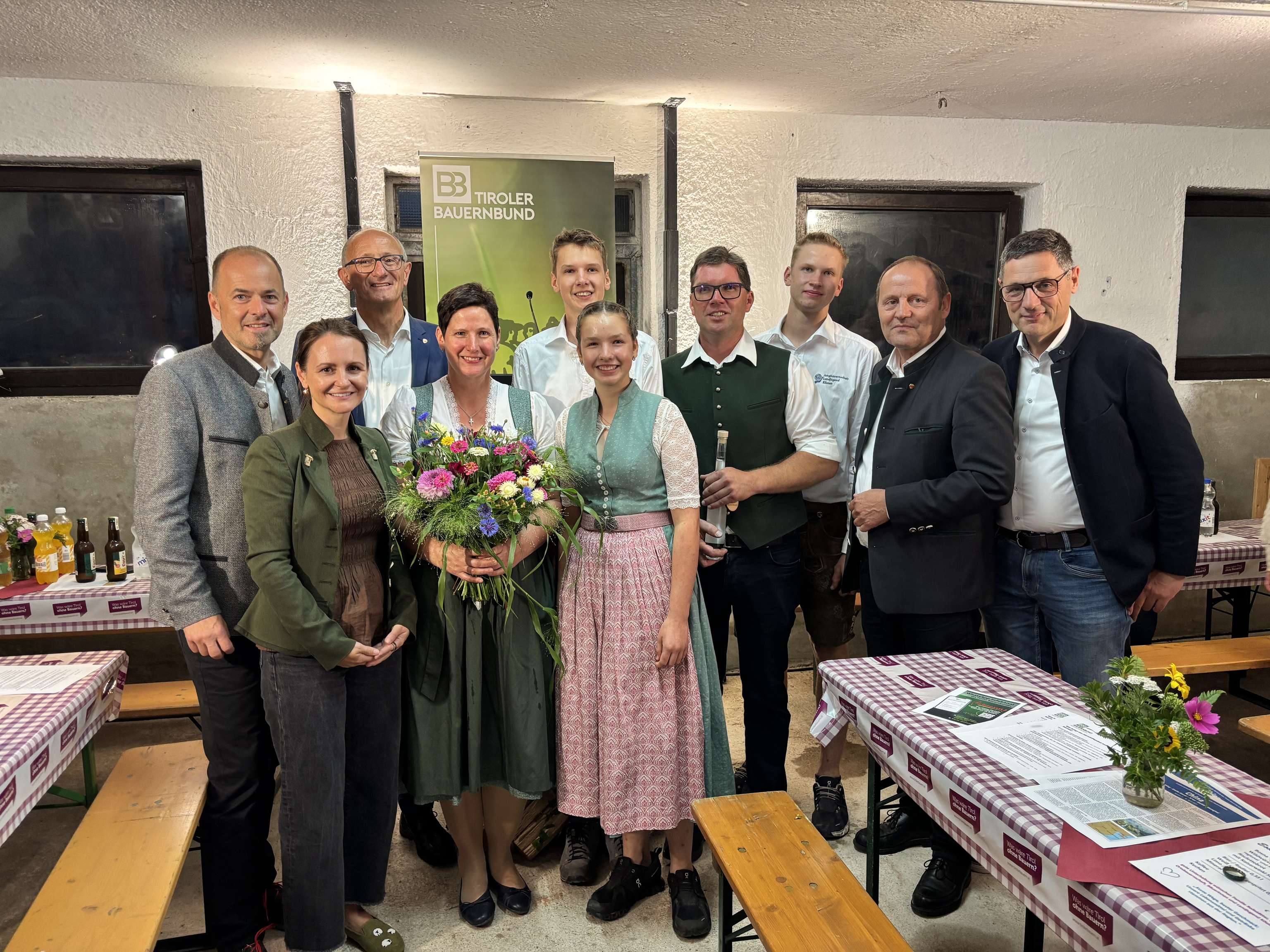 Gruppenfoto beim Tiroler Bauernbund-Event: Personen in Tracht und Businesskleidung, eine Frau hält einen bunten Blumenstrauß.
