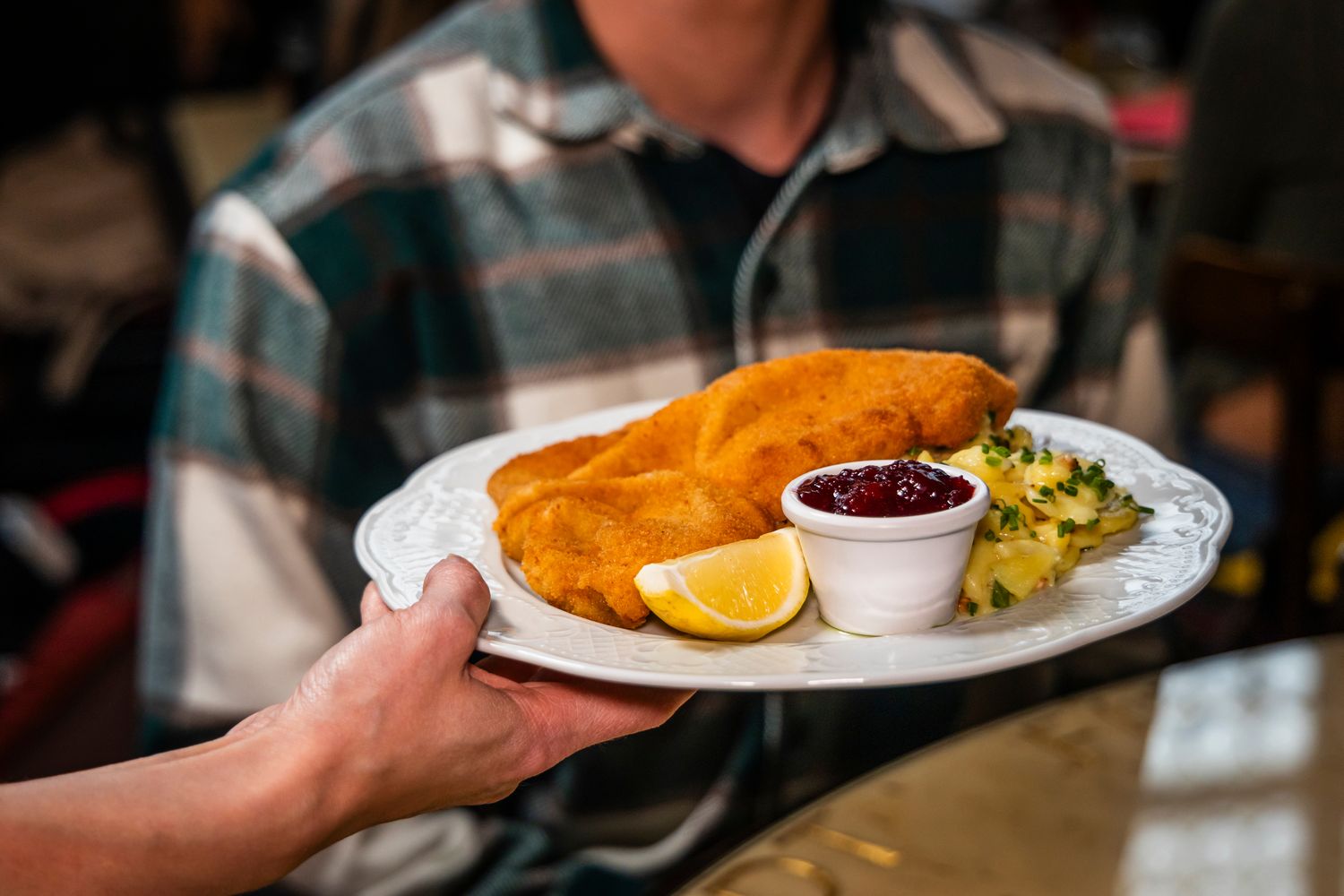 Ein Wiener Schnitzel mit Preiselbeeren und Kartoffelsalat wird serviert
