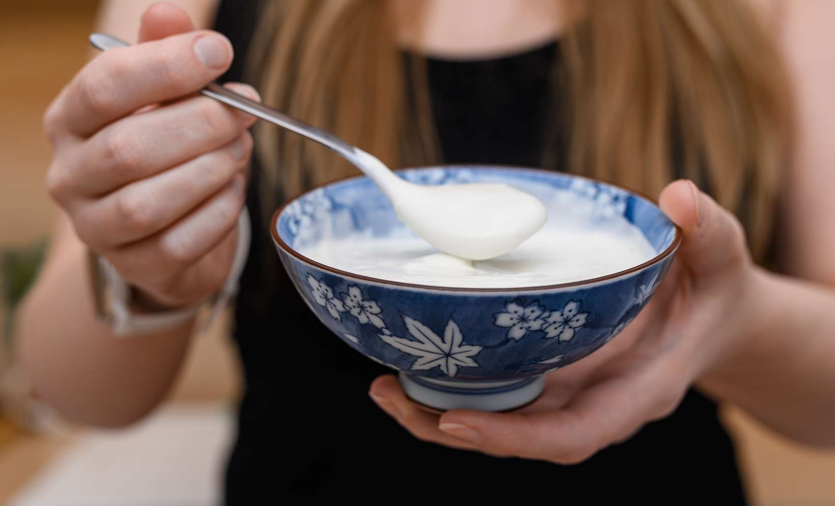 Frau hält eine blaue Schüssel mit weißem Joghurt und einem Löffel in den Händen.