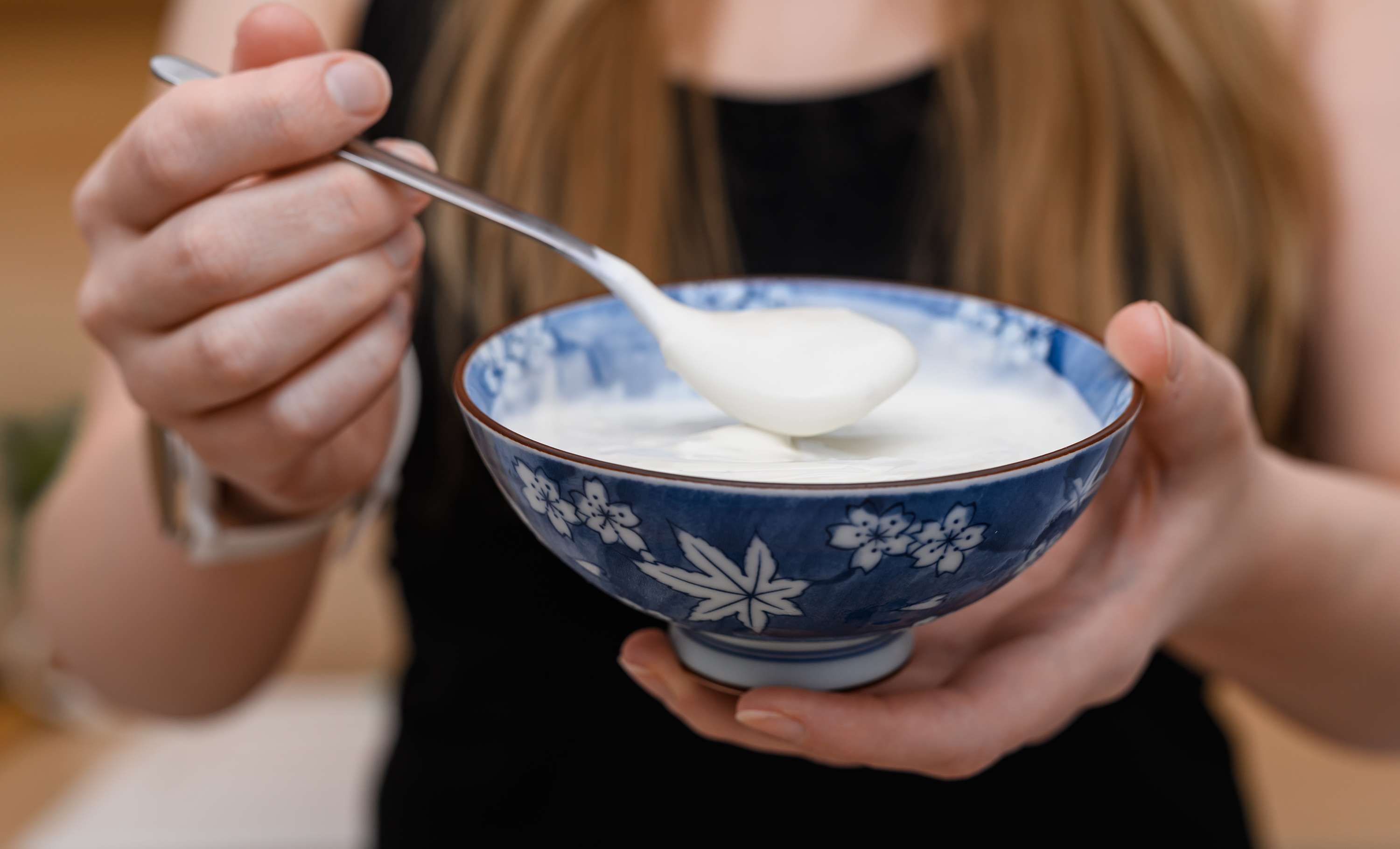 Frau hält eine blaue Schüssel mit weißem Joghurt und einem Löffel in den Händen.
