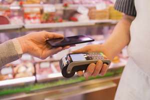 Woman Paying With NFC Technology On Mobile Phone, In Supermarket Butcher