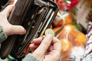 Eine Person zieht einen Euro aus einer Brieftasche vor einem Regal voller Lebensmittel