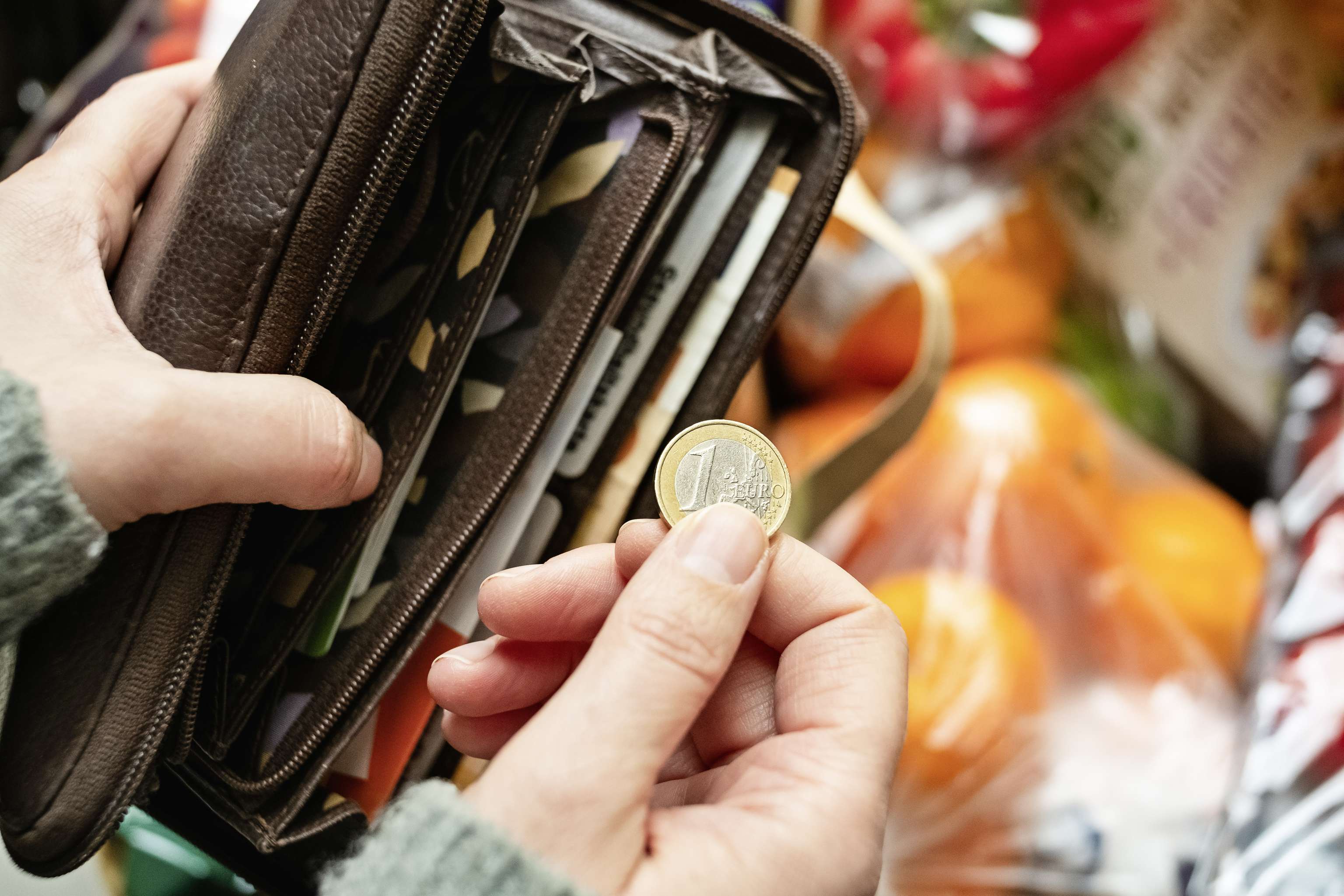 Eine Person zieht einen Euro aus einer Brieftasche vor einem Regal voller Lebensmittel