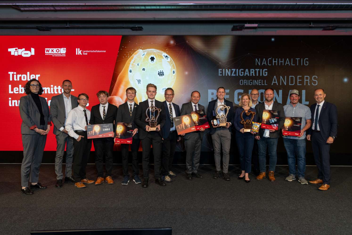 Preisverleihung des Tiroler Lebensmittelinnovationspreises mit Gewinnern und Trophäen vor einer Präsentationswand der WKO Tirol.