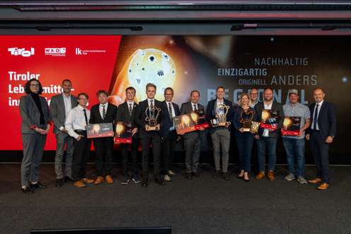 Preisverleihung des Tiroler Lebensmittelinnovationspreises mit Gewinnern und Trophäen vor einer Präsentationswand der WKO Tirol.