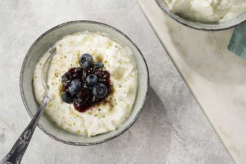 Skyr in einer Schüssel mit frischen Blaubeeren, Beerenmarmelade und Pfeffer, daneben ein Löffel und eine zweite Schüssel.