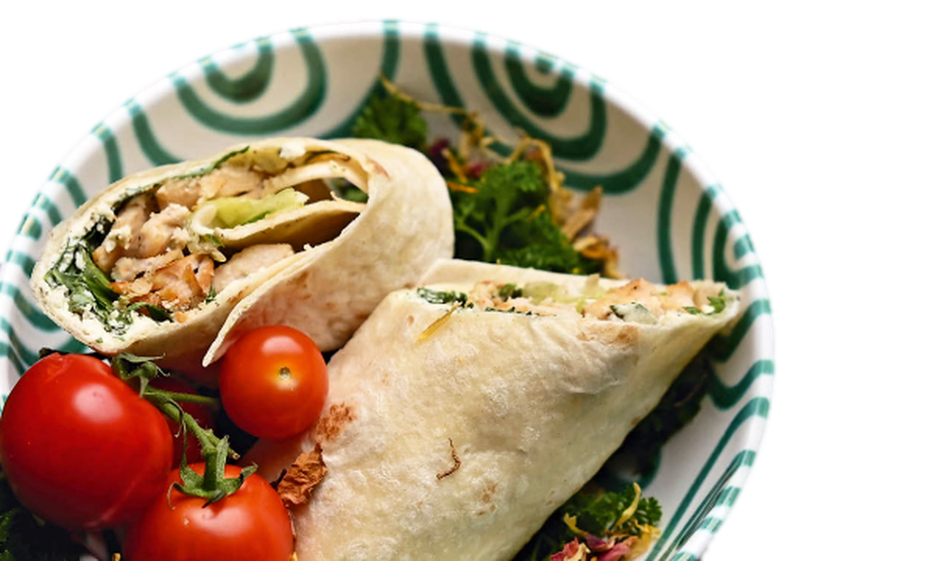 Teller mit gefülltem Wrap, zwei Kirschtomaten und Blattgemüse. Der Wrap enthält Hühnchen und Salat.