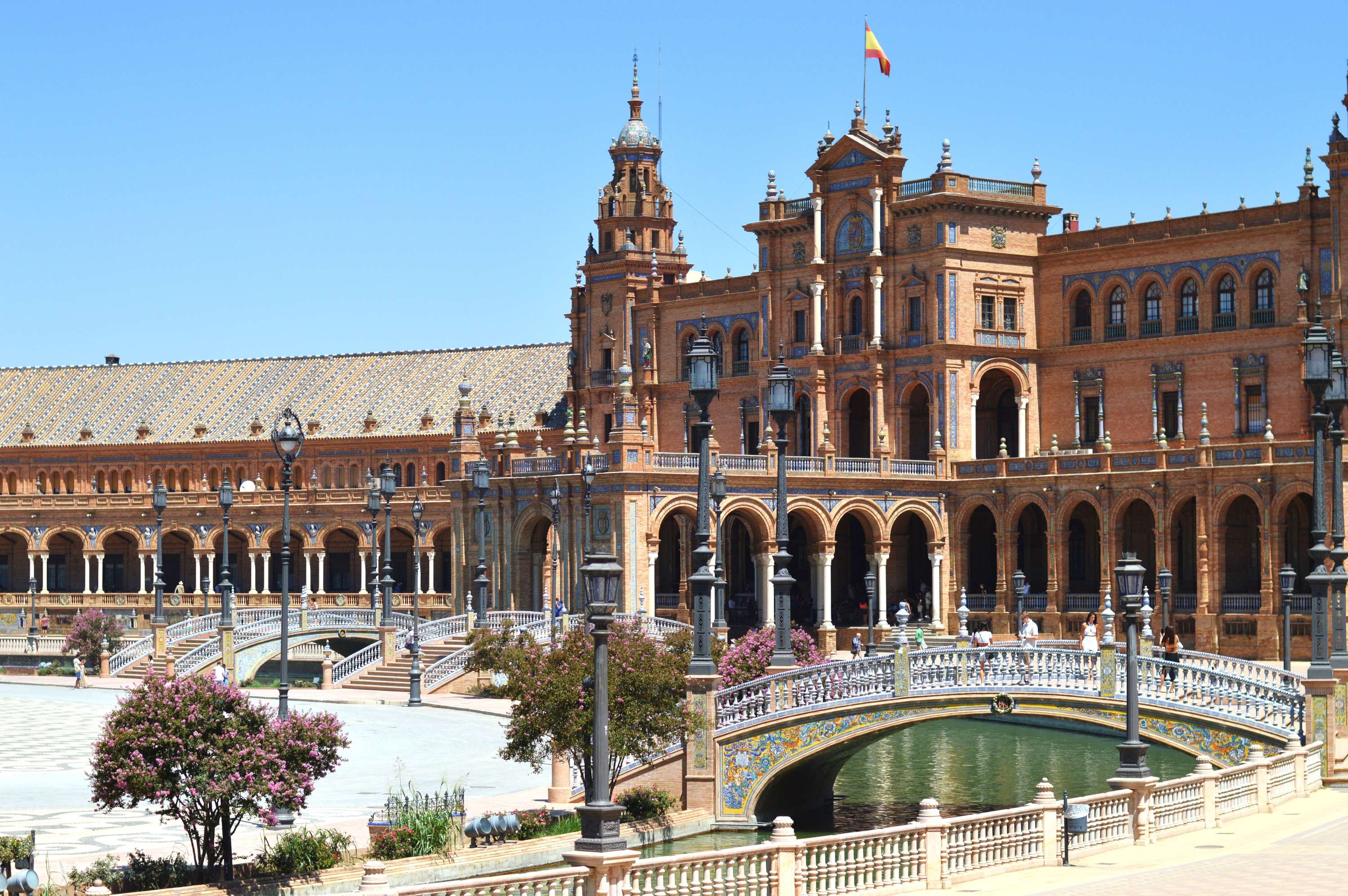 Ansicht des Plaza de España in Sevilla mit beeindruckender Architektur, einem blauen Himmel und einer Brücke über einem kleinen Kanal.