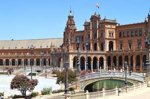 Ansicht des Plaza de España in Sevilla mit beeindruckender Architektur, einem blauen Himmel und einer Brücke über einem kleinen Kanal.
