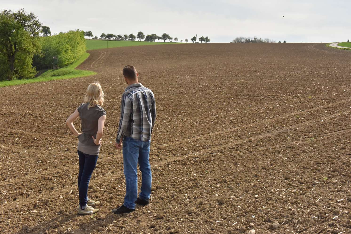 Bäuerin und Bauer blicken auf ein großes Feld.