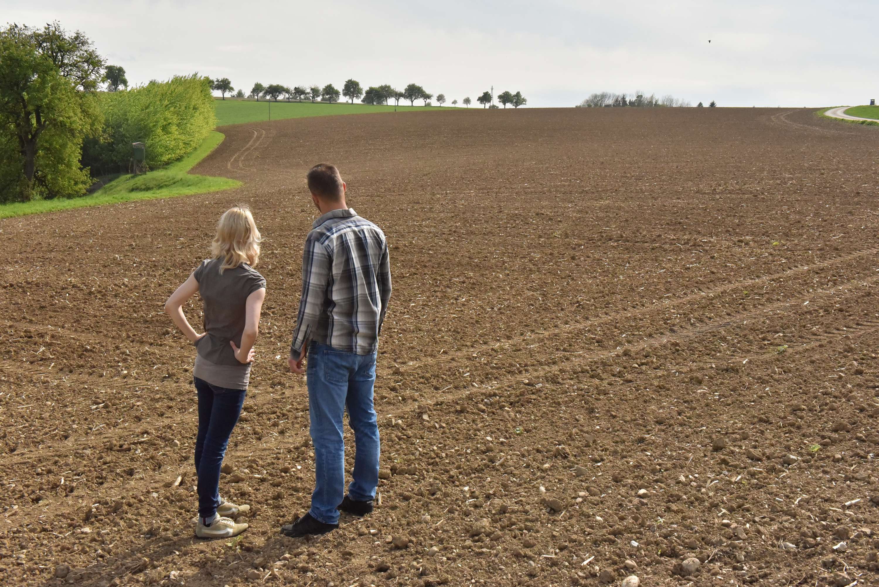 Bäuerin und Bauer blicken auf ein großes Feld.