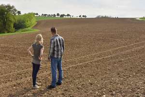 Bäuerin und Bauer blicken auf ein großes Feld.