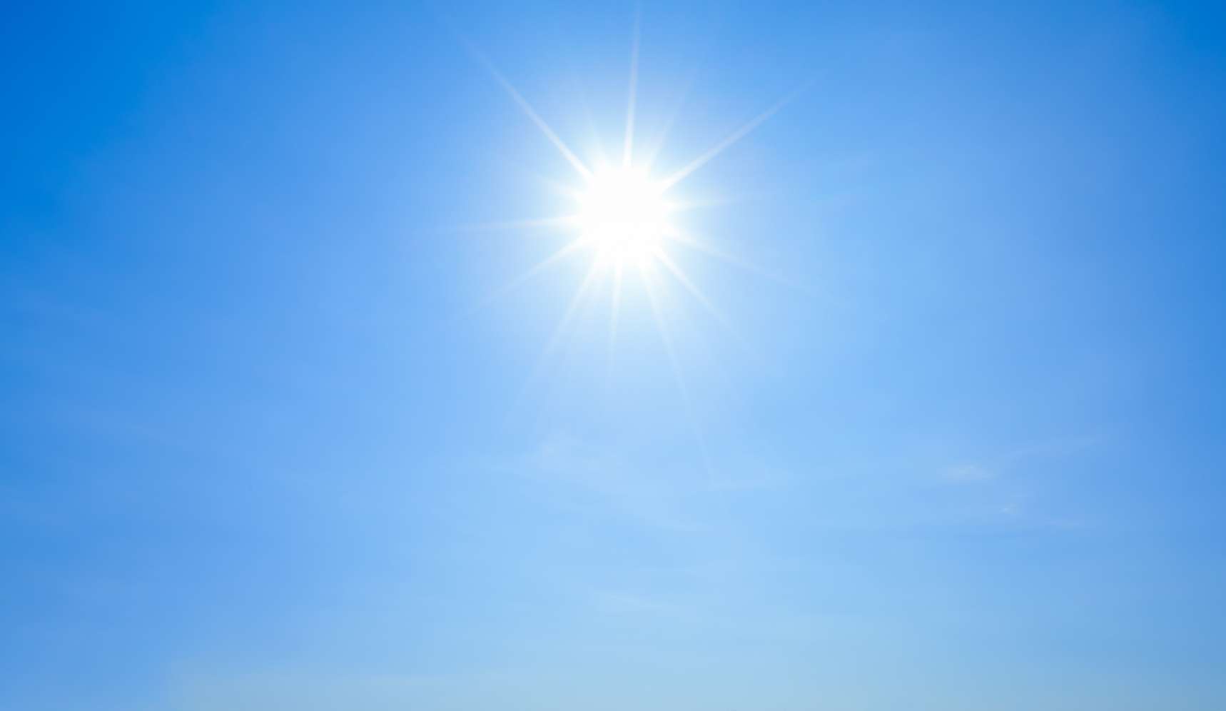 Strahlende Sonne mit Lichtstrahlen am wolkenlosen, hellblauen Himmel an einem sonnigen Tag.