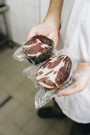 Person hält zwei vakuumverpackte rohe Rindersteaks in Händen, die in durchsichtiger Folie eingewickelt sind. Studiohintergrund.