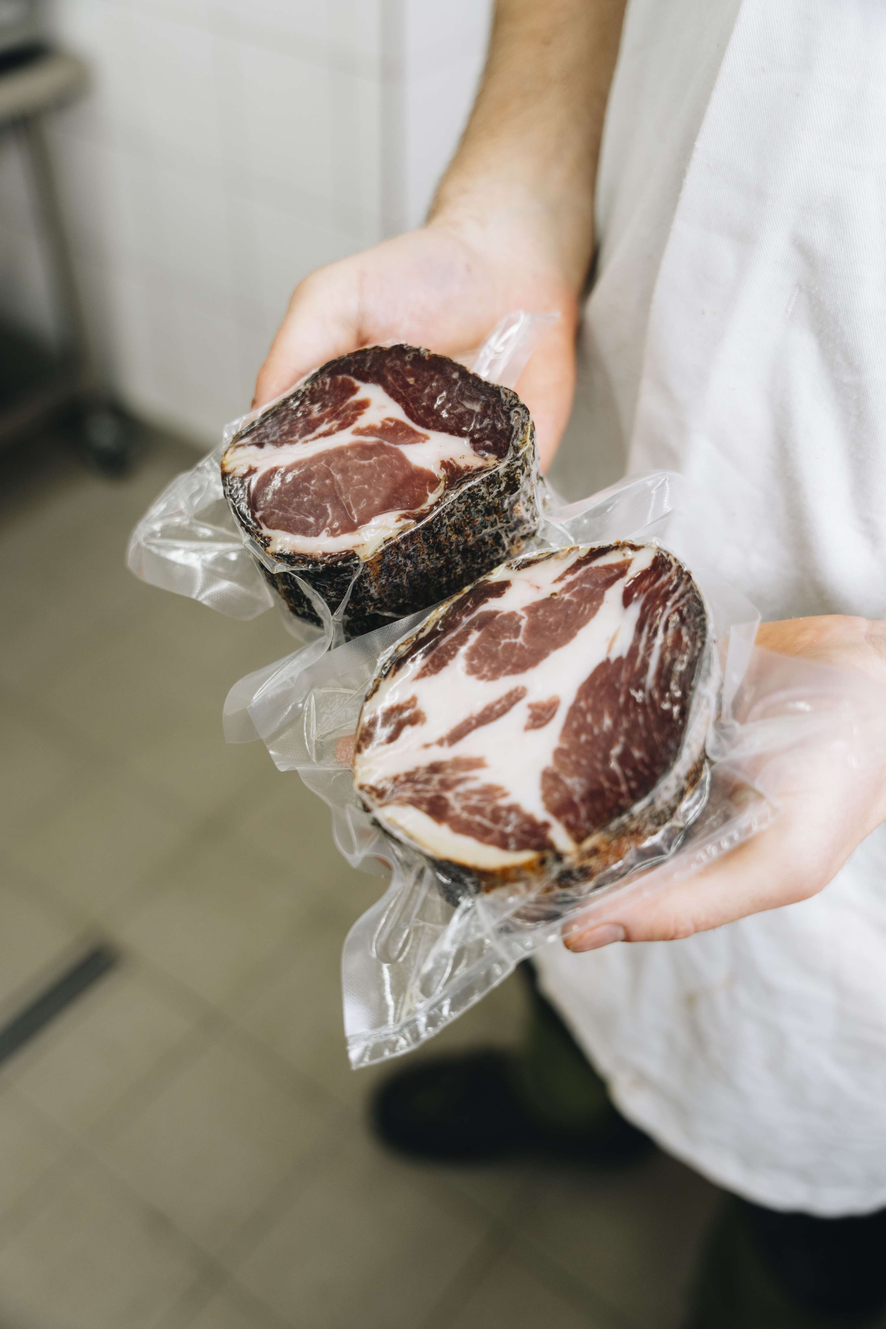 Person hält zwei vakuumverpackte rohe Rindersteaks in Händen, die in durchsichtiger Folie eingewickelt sind. Studiohintergrund.