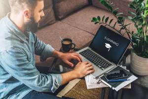 Young Bearded Hipster Man,entrepreneur Sits On Couch At Coffee Table,uses Laptop With Inscription E Learning On Screen