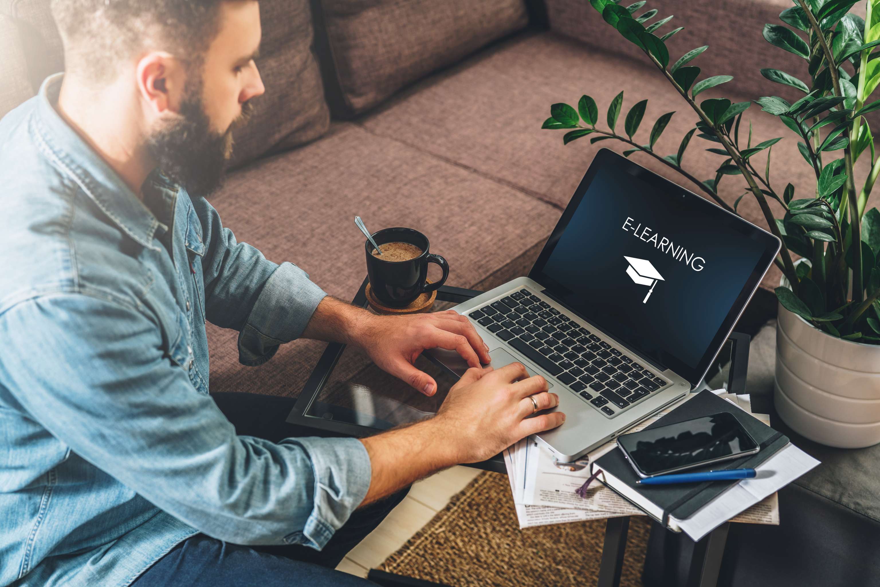 Young Bearded Hipster Man,entrepreneur Sits On Couch At Coffee Table,uses Laptop With Inscription E Learning On Screen
