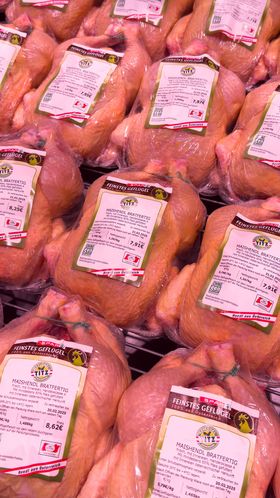 Bratfertige Hühner liegen bei gedämpftem Licht in einer Kühltheke im Supermarkt