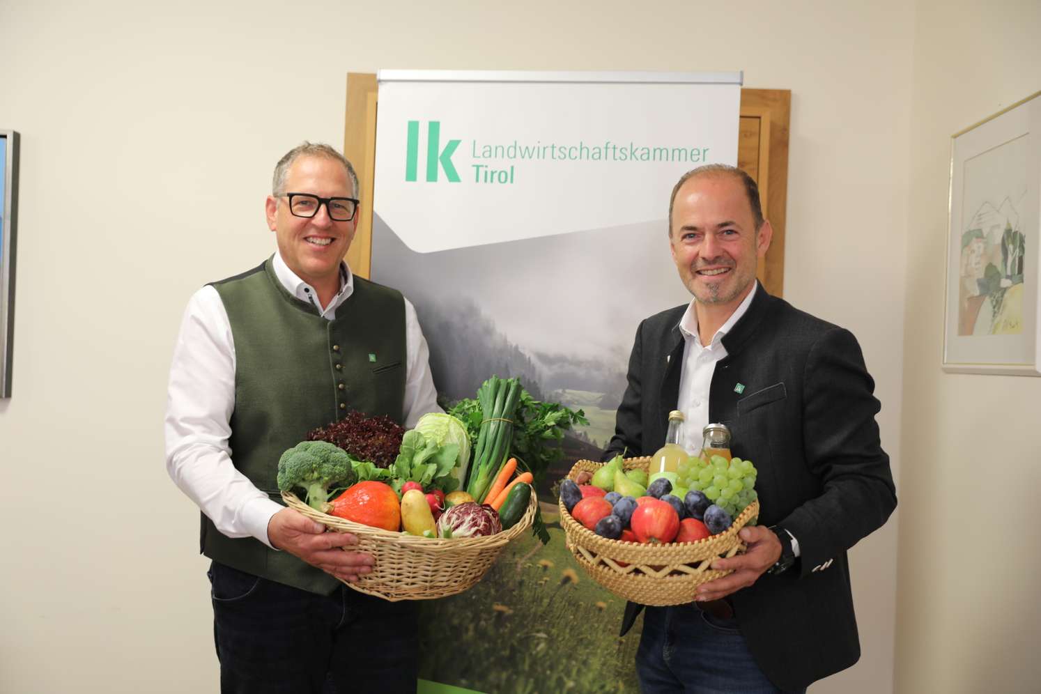 Zwei Männer halten Körbe mit Obst und Gemüse vor dem Logo der Landwirtschaftskammer Tirol.