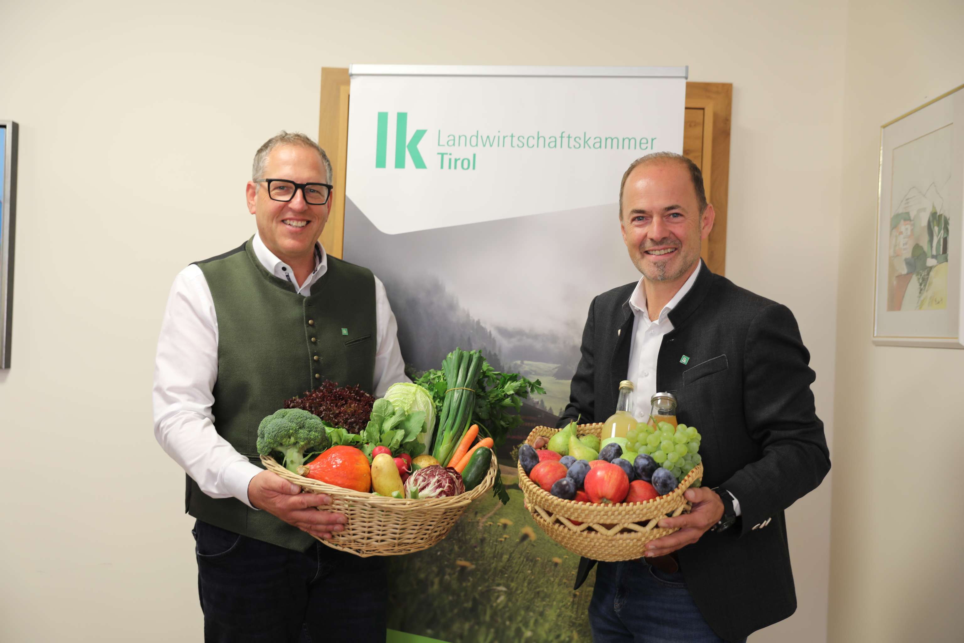 Zwei Männer halten Körbe mit Obst und Gemüse vor dem Logo der Landwirtschaftskammer Tirol.