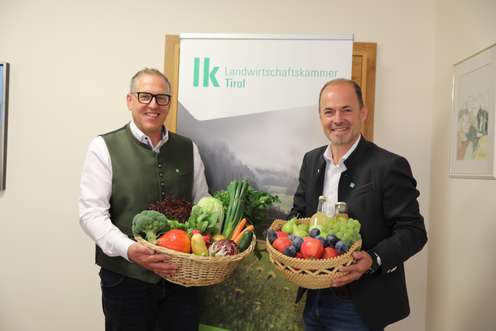 Zwei Männer halten Körbe mit Obst und Gemüse vor dem Logo der Landwirtschaftskammer Tirol.