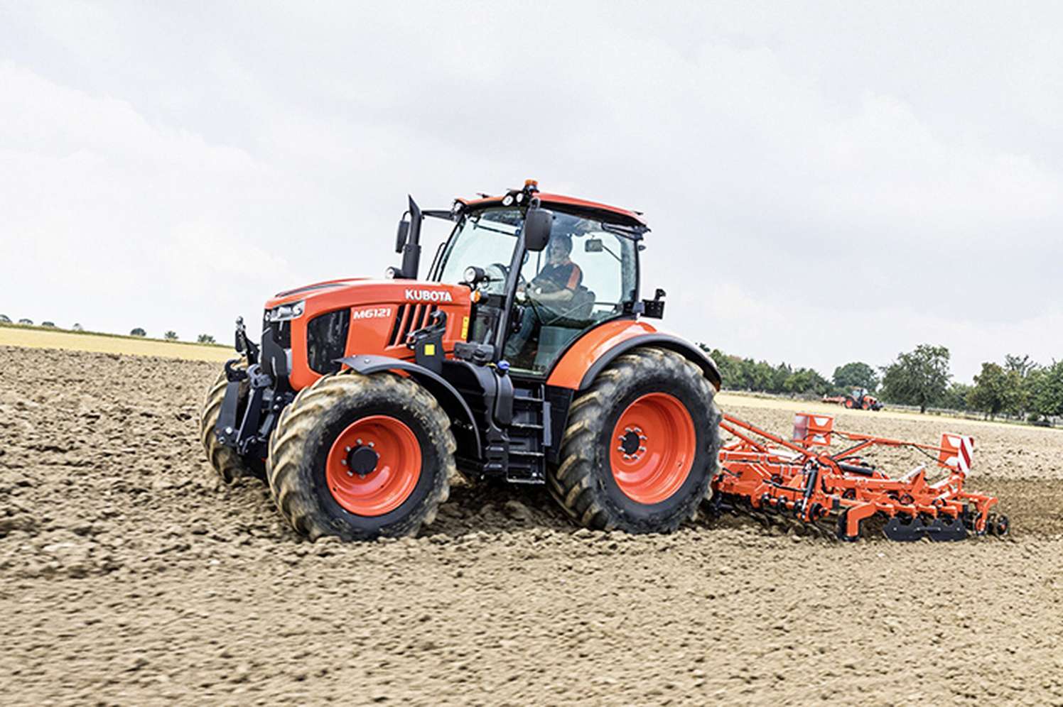 Roter Kubota M6121 Traktor mit Fahrer beim Bodenbearbeiten auf einem Acker mit angehängter Egge.